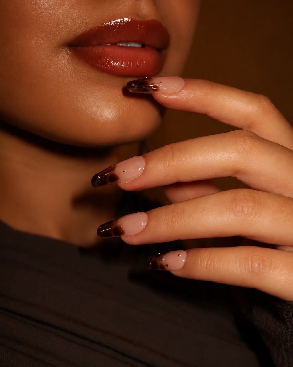Close-up of a person's lips and hand with dark nail polish against a neutral background